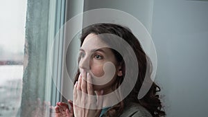 A frightened woman looks out the window at an unpleasant situation, her face is illuminated by the lights of a police