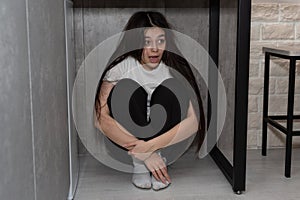 Frightened woman sits under a table and screams because of fear, stress and depression.