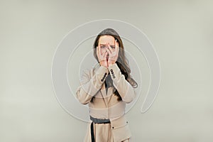 Frightened woman in a suit hid behind her hands and spied, looking at the camera on a beige background with a sad face