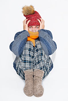 Frightened young handsome man wearing in red hat and blue pullover feeling cold sitting on white background