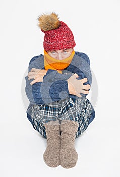 Frightened young handsome man wearing in red hat and blue pullover feeling cold sitting on white background