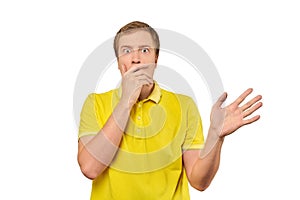 Frightened young man in yellow T-shirt holding hands over face, white background, afraid, negative