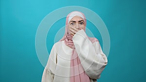 Frightened Young Muslim woman in hijab closing her mouth with hand and looking intimidated scared at camera, gestures no
