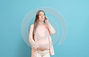 Frightened young pregnant woman on blue background calls by mobile phone, discharge of amniotic fluid, the beginning of labor
