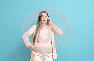 Frightened young pregnant woman on blue background calls by mobile phone, discharge of amniotic fluid, the beginning of labor