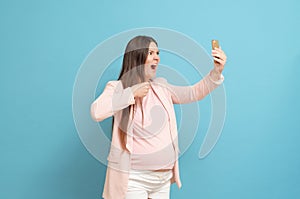 Frightened young pregnant woman on blue background calls by mobile phone, discharge of amniotic fluid, the beginning of labor