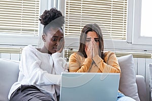 Frightened young women watching movie at home. Girls watching a terror movie on tv sitting on a couch at home. Girlfriends