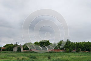 Frightening abandoned and overgrown ruins of agricultural buildings on a rural farm in the fields under a cloudy sky