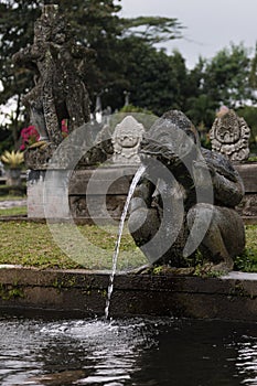 Frightening sculpture of beast or demon of balinese mythology as fountain in majestic park Tirta Gangga on Bali, vertical.