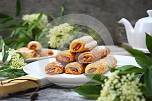 Fripons, French pastries. Apricot jam puff pastry rolls for summer tea and white flowers