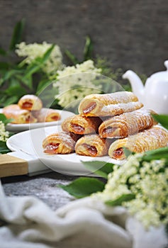 Fripons, French pastries. Apricot jam puff pastry rolls for summer tea and white flowers