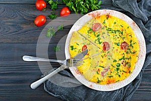 Frittata. Italian omelette with cheese, greens and tomatoes on a white plate on a wooden background.