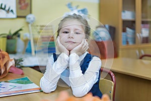 A frivolous schoolgirl of primary classes sits at a desk