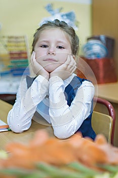 A frivolous schoolgirl of primary classes sits at a desk and listens to a lesson. Day of knowledge. First of September.