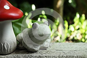 Frog figure and decorative fly agaric on stone parapet outdoors. Space for text