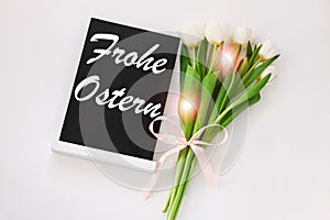 Frohe Ostern means Happy Easter text on black chalkboard with tulip flower on white background,floral spring decorations