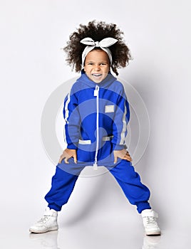 Frolic active mulatto kid girl in warm blue overall jumpsuit stands leaning forward with her hands on knees