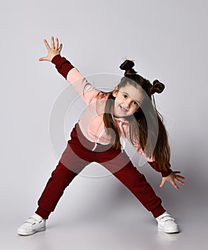 Frolic brunette kid girl in modern fashion pink brown sportwear is bending over with her arms outstretched