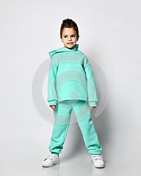 Frolic kid boy with stylish haircut in pastel modern green, mint color hoodie stands calm, quietly waiting, listening