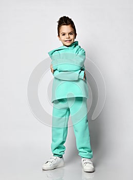 Frolic kid boy with stylish haircut in pastel modern green, mint color hoodie stands hugging himself