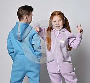 Frolic kids in blue and pink jumpsuits are standing next to each other, boy with his back to us and girl with her face