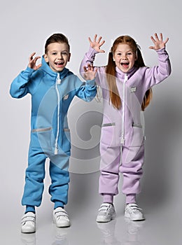 Frolic kids boy and girl in blue and pink jumpsuits stand holding hands up, showing beast claws, playing, scare us