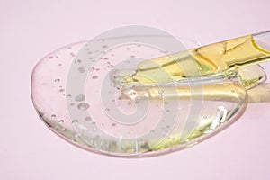 Fron view on pipette with serum or liquid yellow gel on light pink glass background. Beauty cosmetic concept