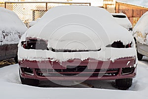 Front of abandoned car covered with snow.