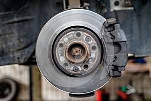 Front brake discs with caliper and brake pads in the car, on a car lift in a workshop.