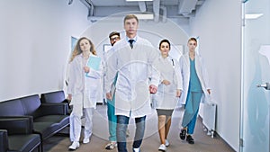 In front of the camera in a modern hospital corridor big team group of doctors and nurses walking in front of the camera
