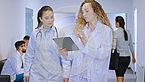 In front of the camera on a modern hospital in the corridor two female doctors analyzing and discussing the diagnostic