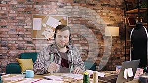 In front of the camera at tailoring atelier good looking man tailor speaks using the headphones with some customer he