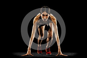 Front camera view of young muscular woman at start line isolated on black background. Sport, track-and-field athletics