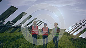 In front of the camera walking group of engineers and investors through the solar panels park they analysing the plan of