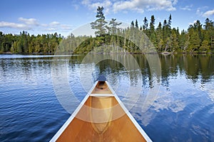 Front of a canoe on a beautiful blue lake with pines and birch on the shore in northern Minnesota