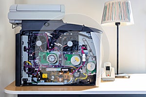 Front close up inside of a office copier machine. Electronic parts and fans. Standing on a desk with a table lamp.