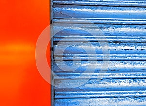 Front closeup of closed blue metal rolling shutter of a shop along with freshly painted red-orange wall