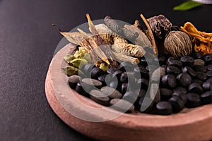 Front closeup shot of black herbal pills, spices and herbs on a grinding stone with black background