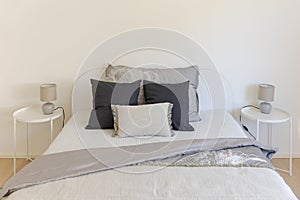 Front detail of a double bed with very large pillows on it and the blankets moved. On the sides there are two comfortable