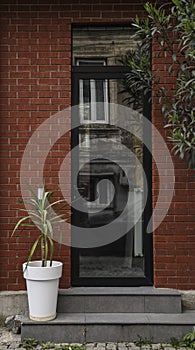 Front door, black front door with brown red wall, light fixtures and green potted plants. Front Door Frame and Greenery. Batumi,