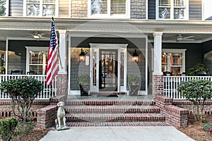 Front door entrance to a large two story blue gray house with wood and vinyl siding and a large American flag.