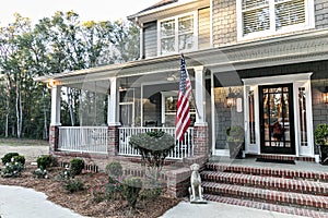 Front door entrance to a large two story blue gray house with wood and vinyl siding and a large American flag.