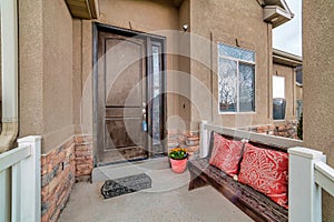 Front door with sidelight of house with bench and potted flowers at the portico