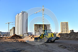 Front-end loader and excavator on road work. Tower crane in action at construction site. Earth-moving heavy equipment for road