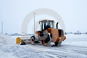 Front end loader works as a snow removal machine clearing a parking lot
