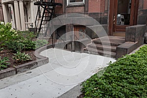 Front entry to old brownstone building with stairs up and down, well maintained landscaping