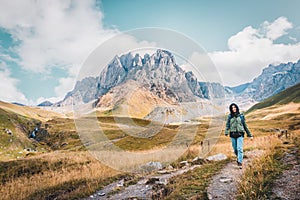 Front happy female caucasian woman hiker walks on pathway in Juta valley with Kazbegi caucasus mountains landscape. KAzbegi