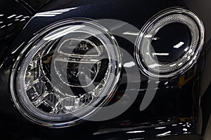 Front headlamp view of black used car stands in the auto showroom sale after washing and polish with led lens in auto service