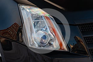 Front headlamp view of black used car stands in the auto showroom sale after washing and polish with orange turn light and bi-xeno
