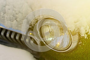 Front headlight of an old car in winter. overgrown with moss. Snowfall